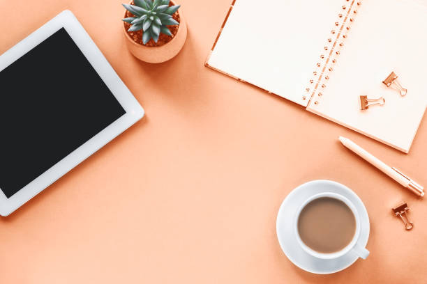 istock Overhead workplace with tablet computer, notepad, pen, coffee cup and succulent plant on peach background 1845723136