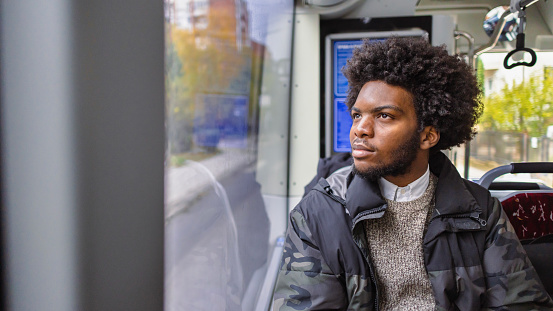 Portrait of a pensive young man of Black ethnicity, looking through the window, while commuting with the public bus
The person can be a refugee, a student, or a person going to work