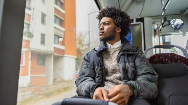 Pensive young man Black ethnicity looking through window, while commuting with a public bus