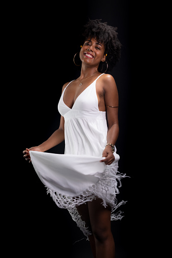 Beautiful beauty, with black power hair, standing moving her white dress against a black background.