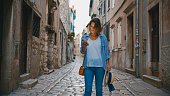 Mid adult female tourist using smart phone while walking on street amidst old buildings at Rovinj,Croatia