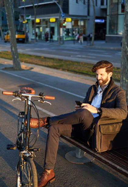 istock Man using phone at sunset in the city sitting on a bench 1845750076