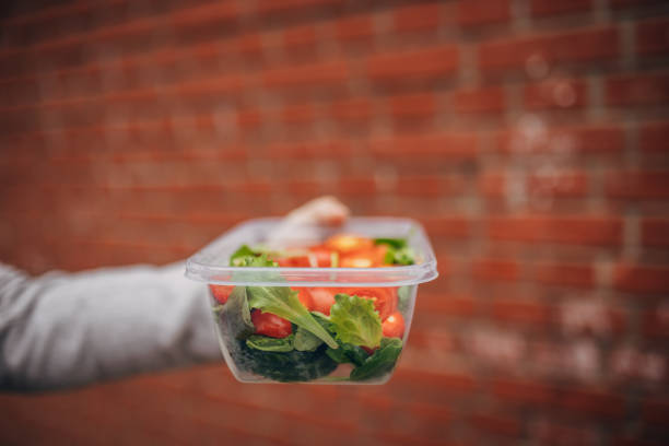 Woman holding plastic food container with vegetable outside in the park
