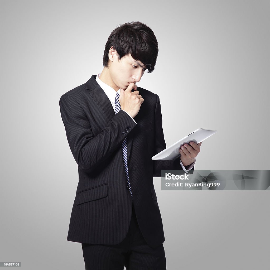 business man reading news on tablet pad young business man is intrigued by the news and reading on his new tablet pad isolated on gray background, asian model Adult Stock Photo