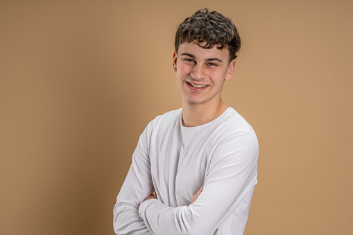 Portrait of one caucasian man 20 years old looking to the camera in front of almond color studio background smiling wearing casual shirt copy space