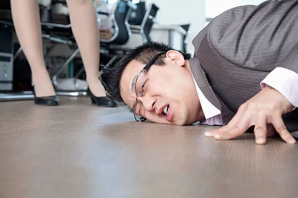 Photo of Businessman with face on the floor, coworker standing by him