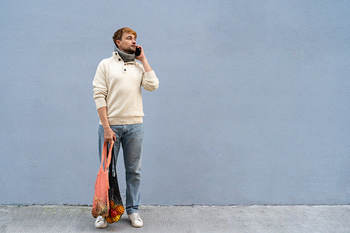 Man using cellphone holding sustainable grocery bags