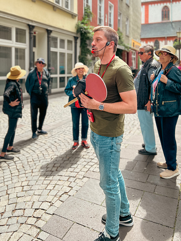 Koblenz, Germany, Europe, July 22, 2023 Handsome tour guide leads a tourist group on a walking tour of the historic city. He is speaking into a microphone head set.