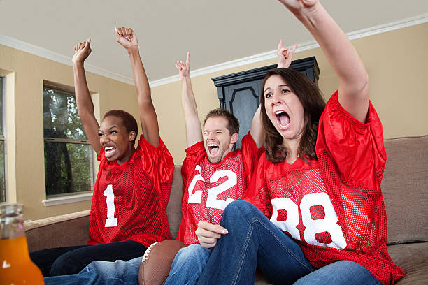 Excited sports fans cheering their football team on at home Excited sports fans cheering their football team on at home. jersey fabric photos stock pictures, royalty-free photos & images