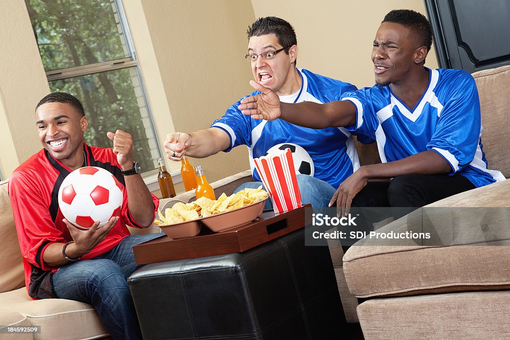 Los aficionados a los juegos de fútbol americano de salón viendo la televisión, malestar con call - Foto de stock de Aclamar libre de derechos