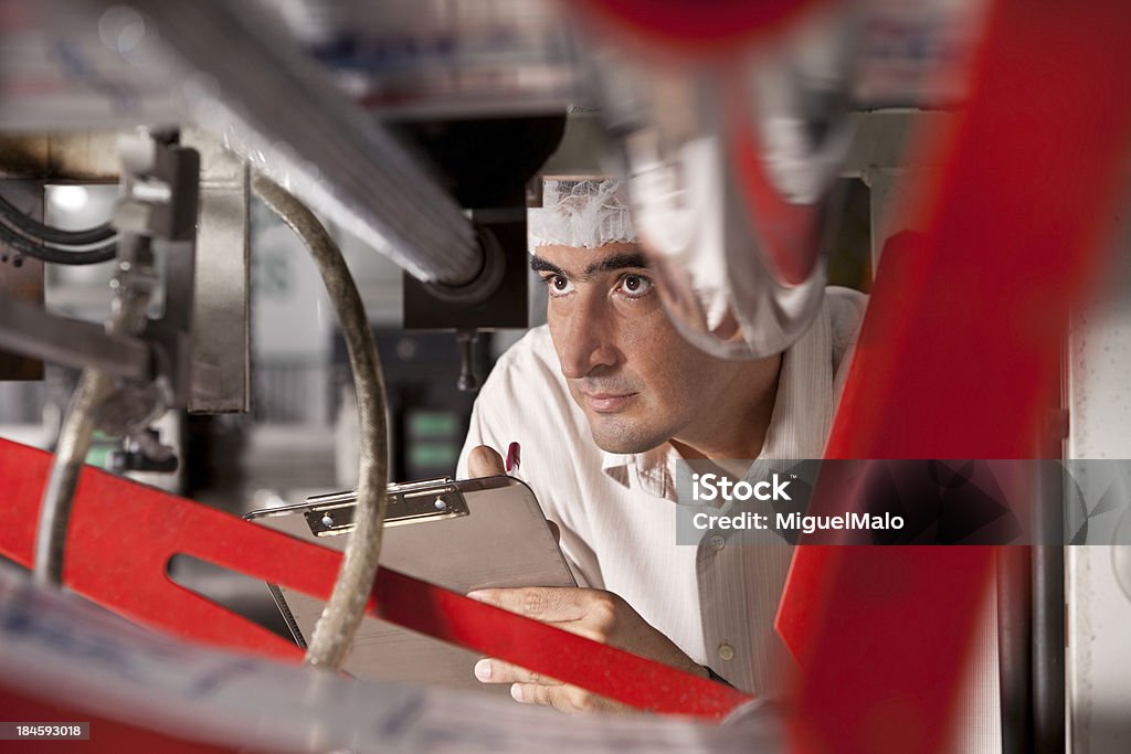 Hombre con portapapeles mirando a través de la máquina - Foto de stock de Fábrica libre de derechos