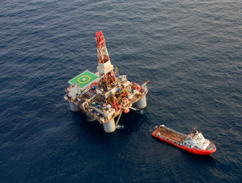 Aerial photograph of a semi-sub oil rig with a large support boat nearby.