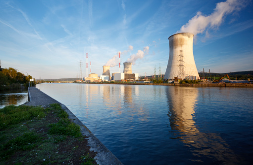 Daytime shot of a nuclear power plant at a river with blue sky and some clouds as well as clean reflection.