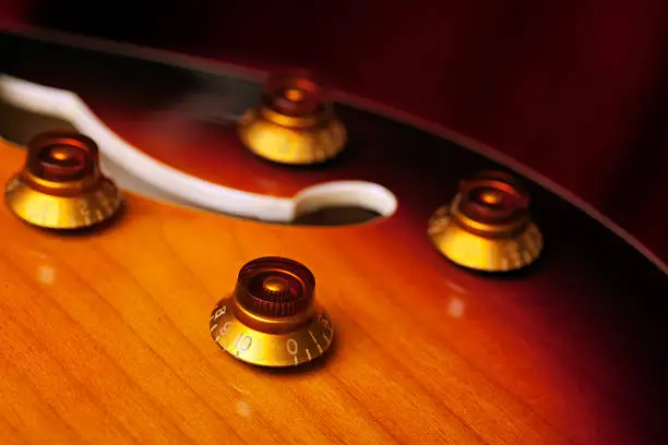 Tone and volume knobs on a sunburst color hollow body electric guitar.