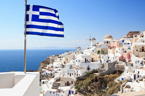 City of Oia on Santorini Island (part of the Cyclades). Old windmills. Greek flag in the foreground.See also