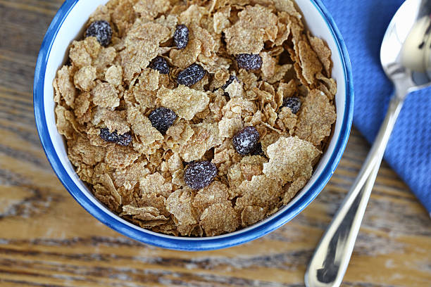 Bran and Raisin Cereal in Blue Bowl Bowl of bran cereal in natural light on table with selective focus on cereal bran stock pictures, royalty-free photos & images