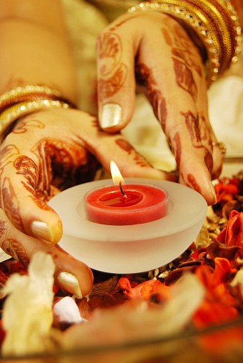 Candle in hands of a female - indian traditional prayer/inauguration - focus on and around wick of candle. Depth of field. Beautiful Henna (tattoo) - religious theme.