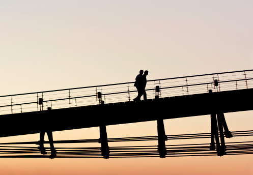 two men crossing a modern steel bridge at dusk