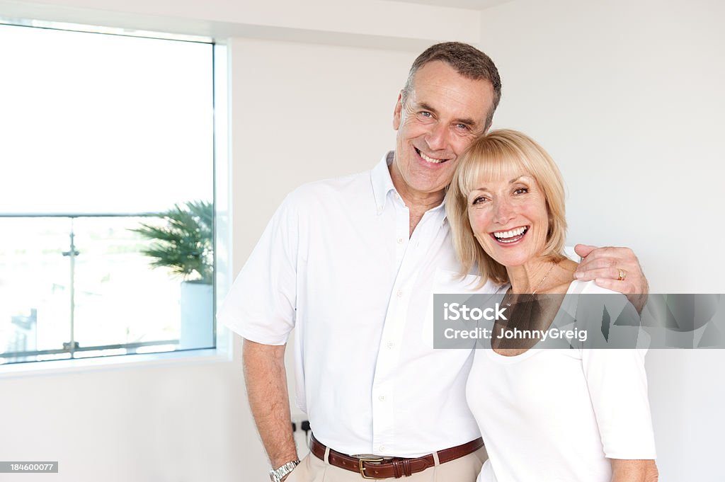 Happy Senior Couple - Indoors Happy caucasian senior couple. Man with his arm around the woman standing and smiling to camera. 60-64 Years Stock Photo
