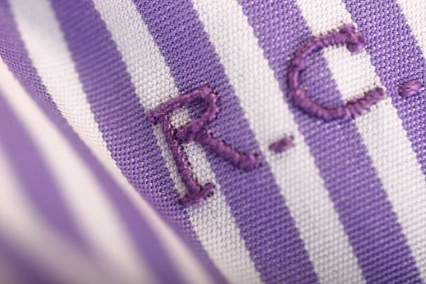 Close-up on the initials embroidered on the front of a handmade, white and purple striped shirt.