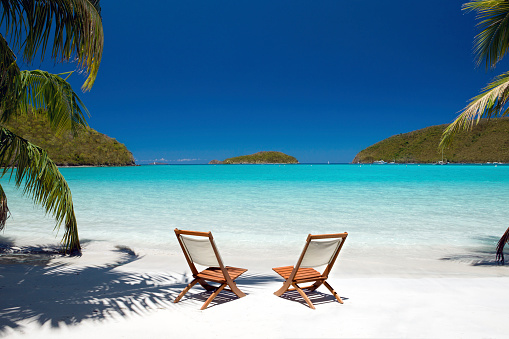 Empty chairs between palm trees at the Virgin Island's beach
