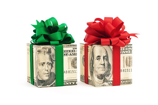 Horizontal view of a group of gift packages wrapped in different U.S. dollar denominations of twenty, and hundred dollar bills, decorated with red and green bows. The bow colors suggest a Christmas gift or bonus. Isolated on a white background.