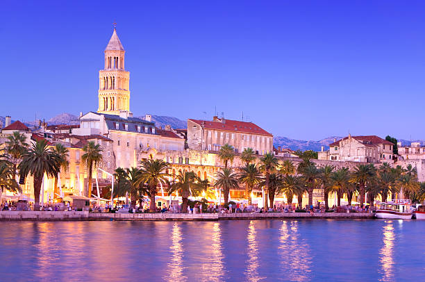 Magical Cityscape of old town Split, Croatia at Dusk "Magical Cityscape of old town Split, Croatia at Dusk with his historic buildings. Visible are sailing boats, Diocletian Palace, city lights, restaurants, coffee bars, hotels and many palm trees. Beautiful night scene with blue sky and their reflection in the water.  See more images like this in:" split croatia stock pictures, royalty-free photos & images