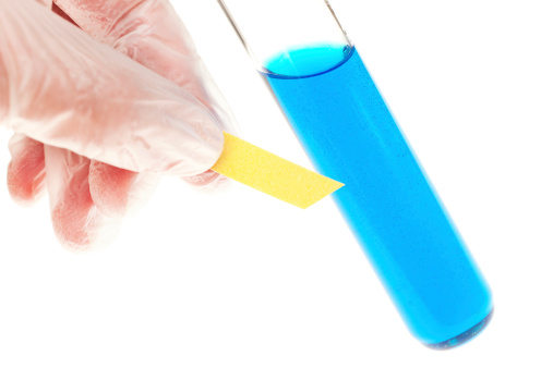 Scientific test using litmus paper on a test tube of blue liquid; isolated on white.