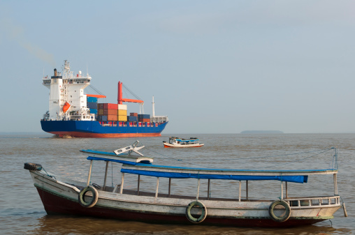 Cargo ship crossing the amazon river with some regional and typical boats on the side