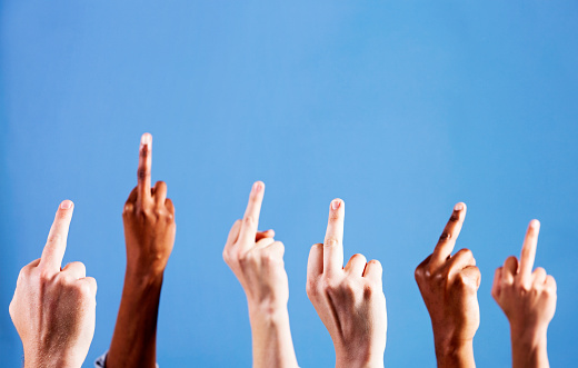 Six mixed hands defiantly give the world the finger, making rude gestures against a sky blue background, with plenty of copy space for your message.