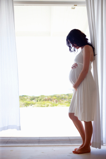 Full length pregnant woman in white dress standing at home