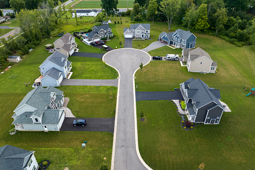 Aerial view of private residential houses in rural suburban sprawl area in Rochester, New York. Upscale suburban homes with large backyards and green grassy lawns in summer season.