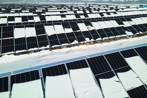 Aerial view of snow melting from covered solar photovoltaic panels at sustainable electric power plant for producing clean electrical energy. Low effectivity of renewable electricity in winter.