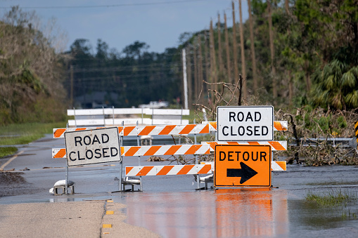 Hurricane flooded street with road closed signs blocking driving of cars. Safety of transportation during natural disaster concept.