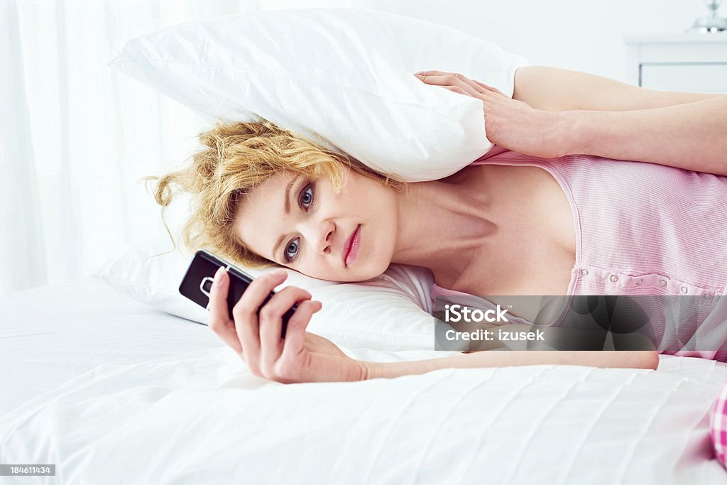 Waiting for a message Young adult woman lying in a bed and looking at the cell phone - waiting for an important message or just checking time. 25-29 Years Stock Photo