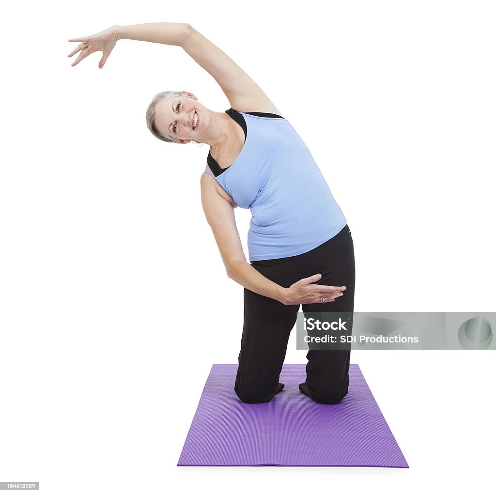 Anziani donna stretching al braccio oltre il tappetino da yoga - Foto stock royalty-free di Abbigliamento sportivo