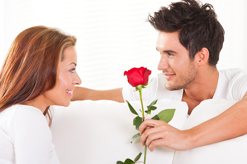 Teen boy gives his girlfriend a bouquet of red roses on a white background. First love concept. Studio photography.