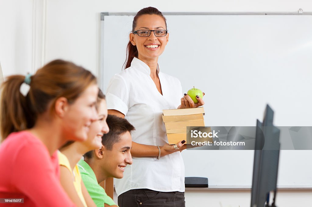 Profesor sonriente con libros en la computadora de la clase - Foto de stock de Delante de libre de derechos