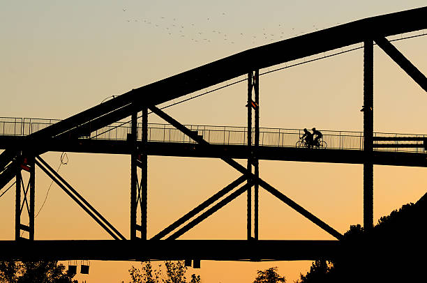 Two cyclist in silhouette ride across the Clinton Library Bridge (Rock Island Bridge) at sunrise.