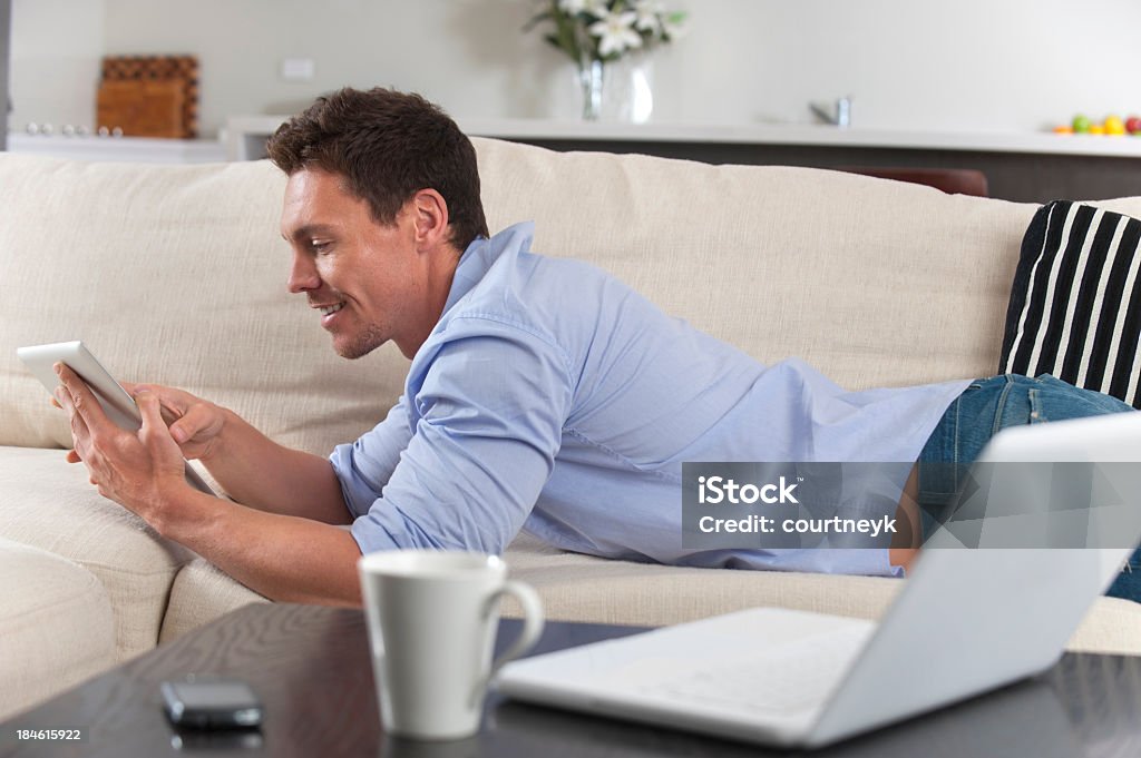 Sonriente hombre usando una tableta digital descansar en el sofá cama - Foto de stock de 20-24 años libre de derechos
