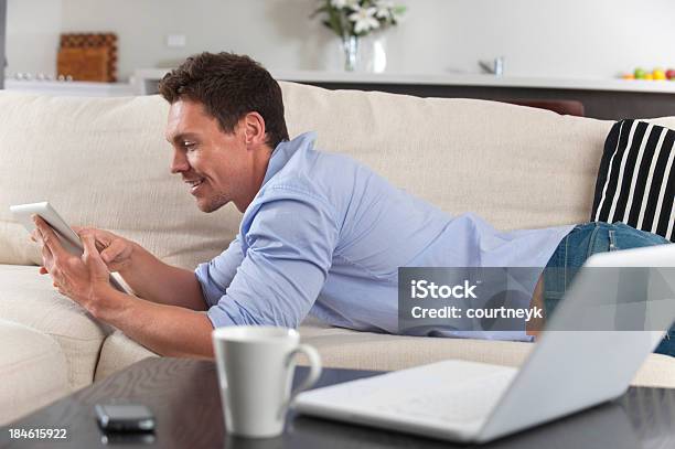 Foto de Homem Sorridente Usando Um Tablet Deitado No Sofá e mais fotos de stock de 20-24 Anos - 20-24 Anos, 25-30 Anos, 30 Anos