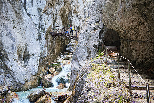 Unidentifiable hikers in the Hoellentalklamm. The Hoellentalklamm (free translation to english: Hells Valley Gorge) near Grainau, Garmisch-Partenkirchen, is a wild and spectacular hike along the creek Hammersbach at the highest mountain of Germany, the Zugspitze. There are deep crevices, waterfalls, canyons. Supported by passenger tunnels, man made steps and bridges this 1km long gorge is accessible also to untrained hikers.
