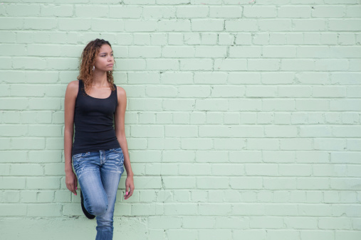 A cute young woman leaning against a wall. Plenty of copy space.