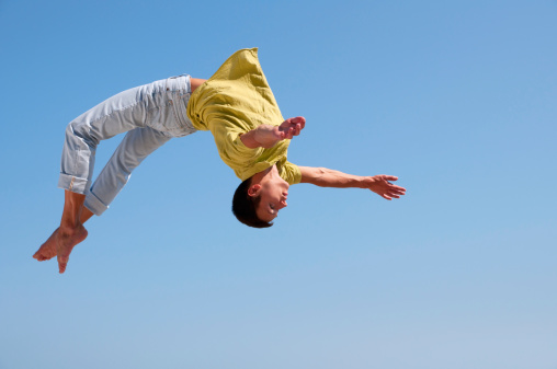 Young man doing a somersault on the background of blue sky