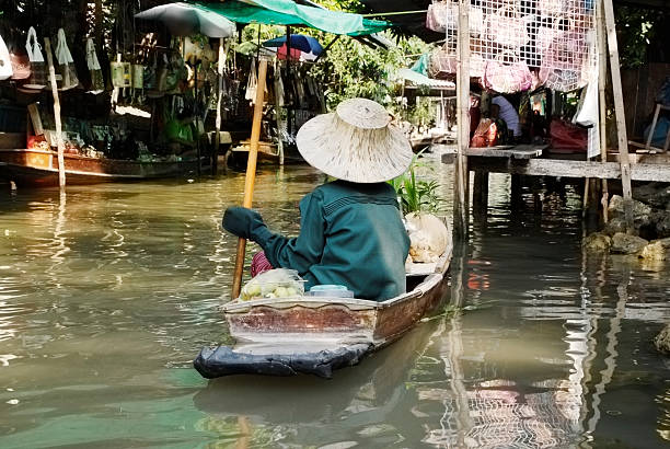 istock Lady punting boat through floating market in Thailand 184616890