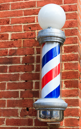 An old fashioned red, white and blue barbershop pole hanging on an old red brick wall.