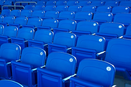 Rows of blue and grey empty plastic seats on the stands of a sports stadium on a summer day