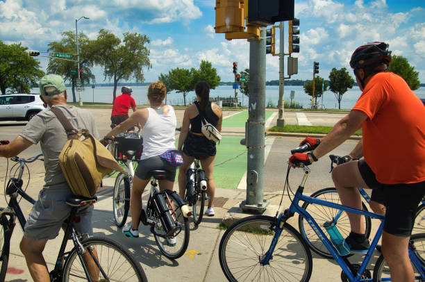 On a Summer day in Madison, WI, bikers wait to cross a busy street on a trail near Lake Monona.