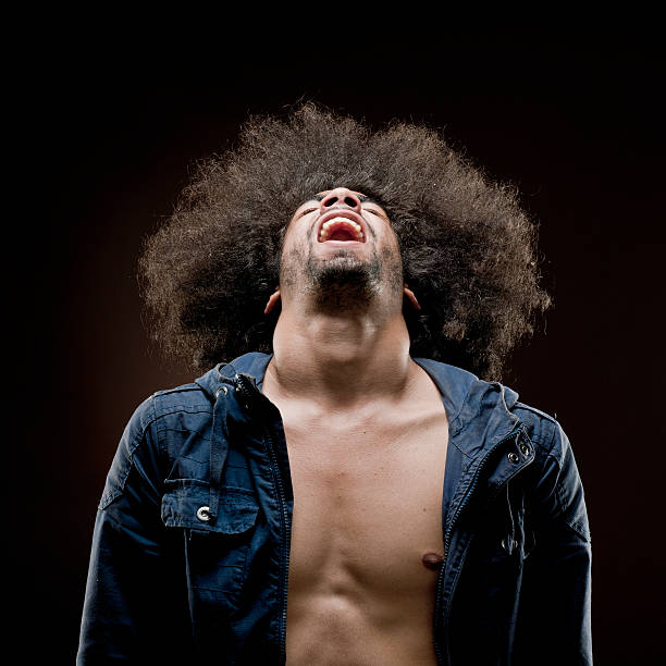 waist up shot of a hysterical screaming man with big afro hair and beard in fully unbuttoned blue shirt on black background