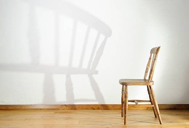 Old wooden chair casting shadow on wall stock photo